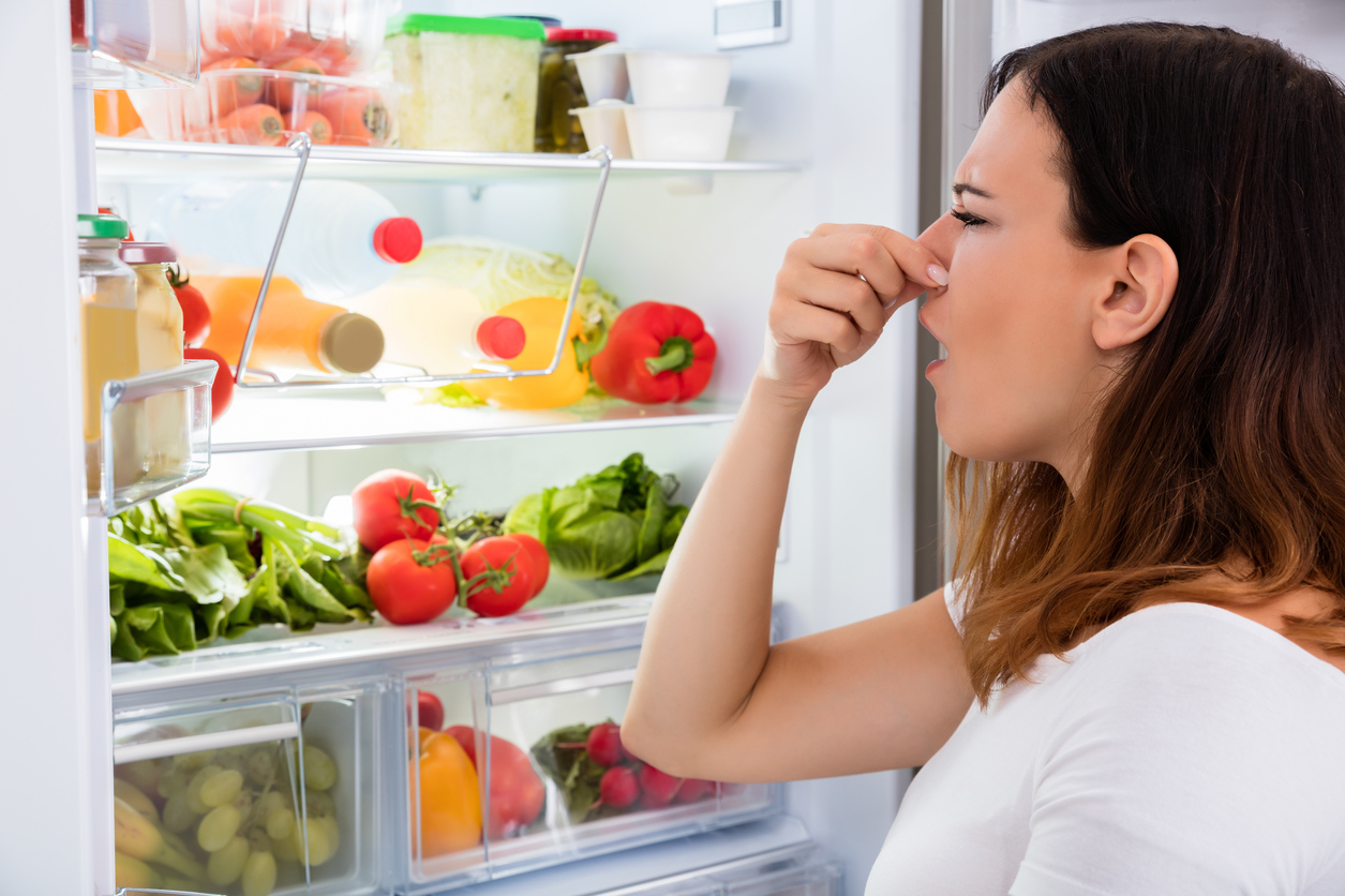 Mujer tapando nariz refrigerador abierto